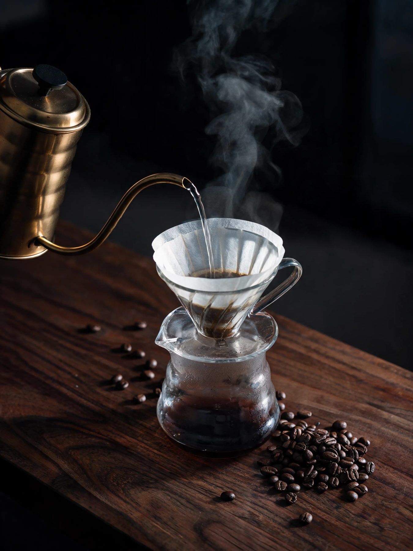 Gooseneck kettle pouring into a glass dripper on a dark walnut counter